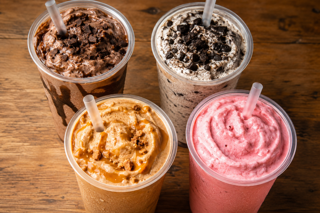 Four thick Cook Out milkshakes in chocolate, Oreo, caramel, and strawberry flavors displayed side by side
