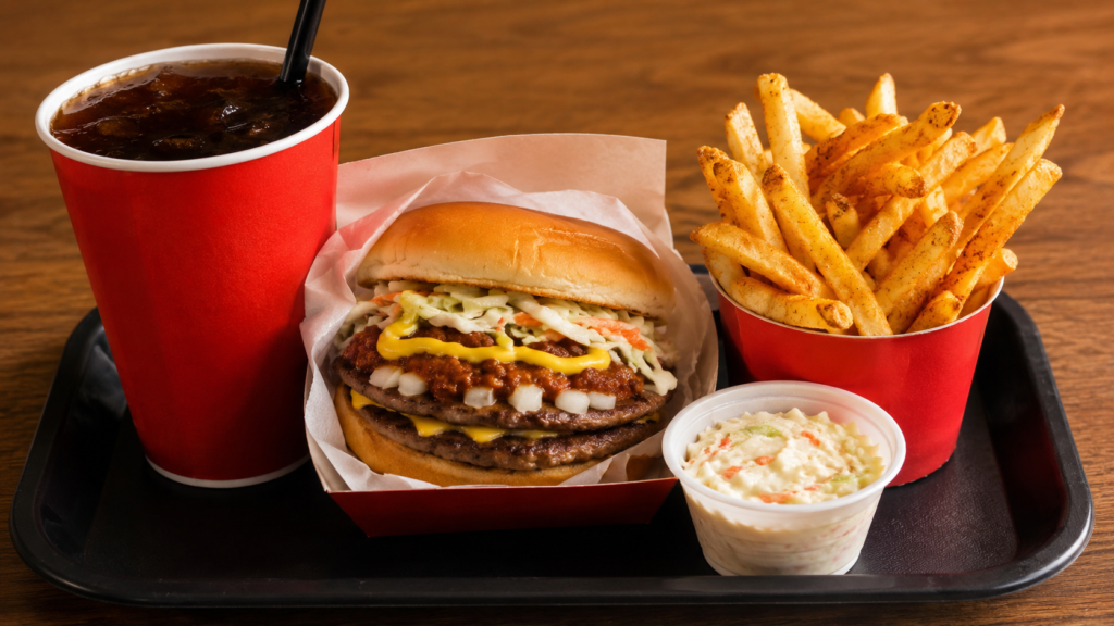Cook Out Tray meal showing a double burger, Cajun fries, coleslaw, and a large drink on a wooden surface